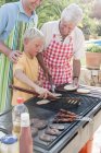 Boy cooking kebabs and burgers on barbecue with father and grandfather — Stock Photo