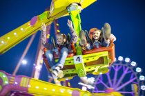 Sister and brother mid air on fairground ride at night — Stock Photo