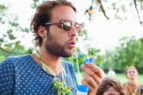 Young man blowing bubbles at sunset party in park — Stock Photo