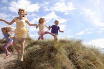 Мать с тремя детьми, прыгающая с дюн, Уэльс, Великобритания — стоковое фото