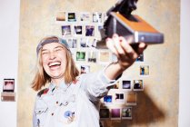 Молода жінка перед фотошпалерами приймає миттєве селфі на ретро камеру — стокове фото