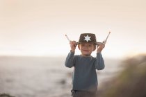 Niño vestido de vaquero sheriff sosteniendo el sombrero y armas de juguete en dunas de arena - foto de stock