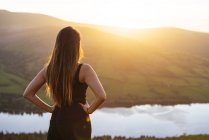 Vista posteriore di una giovane donna che si affaccia sul Talybont Reservoir nella valle di Glyn Collwn, Brecon Beacons, Powys, Galles — Foto stock