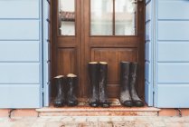 Trois paires de bottes en caoutchouc sur le pas de la porte — Photo de stock