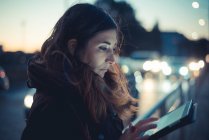 Mitte erwachsene Frau mit digitalem Tablet-Touchscreen in der Abenddämmerung auf der Straße — Stockfoto