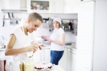 Woman icing homemade cake in kitchen — Stock Photo