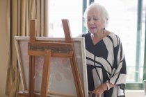 Mulher sênior pintura arte lona na aposentadoria villa — Fotografia de Stock