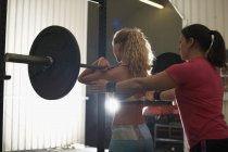 Trainer coaching woman with barbell in gym — Stock Photo