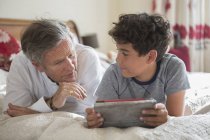 Senior und Enkel entspannen sich im Bett, schauen auf das digitale Tablet — Stockfoto