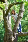 Sorridente ragazza arrampicata albero all'aperto — Foto stock