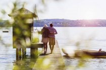 Вид сзади на молодую пару, идущую вдоль озера к лодке, Озил, Аммерзее, Бавария, Германия — стоковое фото