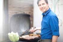 Mature man barbecuing sausages — Stock Photo