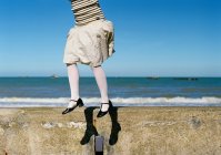Girl jumping on stone wall at beach — Stock Photo