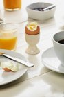 Boiled egg in eggcup with glass of orange juice and coffee cup — Stock Photo