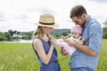 Parents holding baby daughter in field — Stock Photo