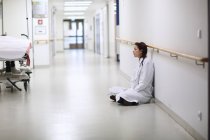 Female doctor sitting cross legged in hospital corridor — Stock Photo