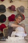 Milliner attaching decoration to hat in shop — Stock Photo