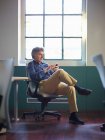 Reifer Geschäftsmann sitzt mit Handy auf Bürostuhl — Stockfoto