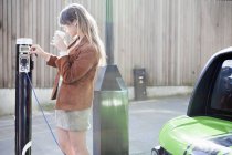 Жінка заряджає електромобіль на вулиці — стокове фото