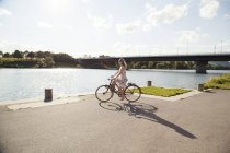 Jeune femme faisant du vélo au bord de la rivière, île du Danube, Vienne, Autriche — Photo de stock