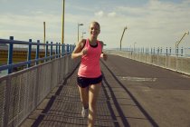 Jeune joggeuse courir sur le pont — Photo de stock