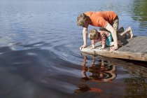 Отец и сын смотрят в озерную воду с пирса, Сомерниеми, Финляндия — стоковое фото