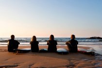 Cuatro personas sentadas en la playa - foto de stock