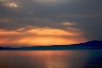 Golden sunset light in cloudy sky above sea and mountains — Stock Photo