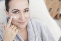 Mature woman applying moisturiser to face — Stock Photo