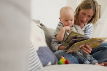 Reife Mutter und kleine Tochter auf dem Sofa im Wohnzimmer lesen Bilderbuch — Stockfoto