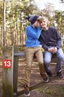 Twin brothers sitting and whispering on gate in forest — Stock Photo
