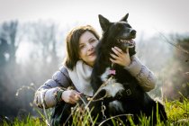Retrato de mujer adulta con brazo alrededor de su perro en el campo - foto de stock