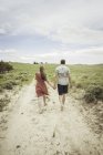 Rear view of young couple walking barefoot along sandy track, Cody, Wyoming, USA — Stock Photo