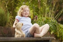 Girl on garden seat with teddy bear and star stickers on legs — Stock Photo