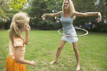 Girl watching mother hula hooping on green lawn — Stock Photo