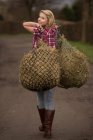 Teenage girl carrying hay on dirt path — Stock Photo