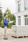 Full length side view of architect holding plans looking at house exterior — Stock Photo