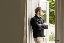 Homem adulto médio olhando para fora da janela, braços dobrados — Fotografia de Stock