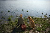 Garçon pêche avec chien sur la rivière, vue arrière — Photo de stock