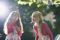 Two girls blowing bubbles in sunlit garden — Stock Photo