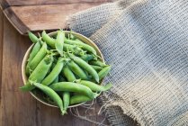 Bowl of green peas on table with burlap — Stock Photo
