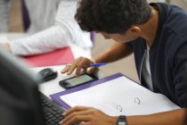 Junge männliche College-Studenten am Computertisch, die auf dem Smartphone rechnen — Stockfoto
