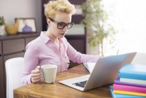 Mujer usando laptop y tomando café en el escritorio - foto de stock