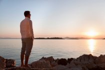 Uomo guardando il sole tramontare sulla spiaggia rocciosa — Foto stock