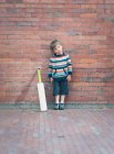 Menino com bastão de críquete contra parede de tijolo — Fotografia de Stock