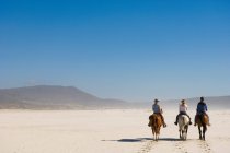 3 personnes à cheval sur la plage — Photo de stock