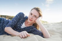 Дівчина-підліток лежить на пляжному піску і дивиться на камеру — стокове фото