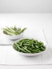 Judías verdes crudas en la tabla de cortar y tazón de judías verdes hervidas - foto de stock