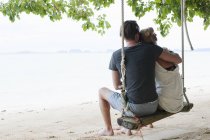 Вид сзади на молодую пару, сидящую на пляжных качелях, Федан, Таиланд — стоковое фото