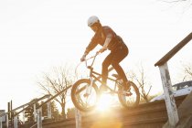 Female BMX rider riding down sunlit stairway — Stock Photo